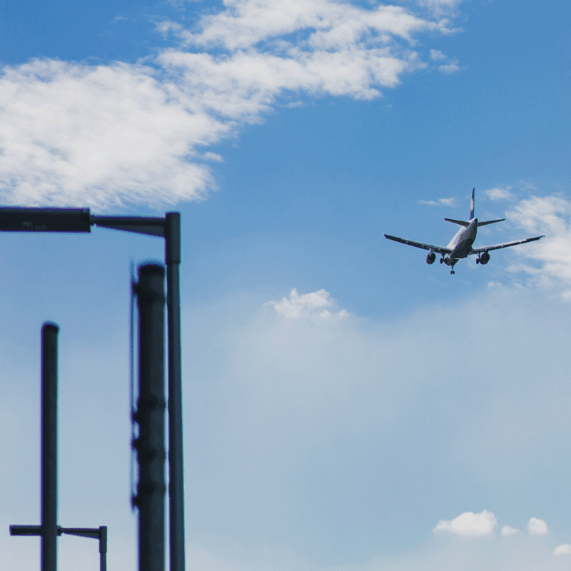 Airplane flying in a clear blue sky near buildings, symbolizing air travel.