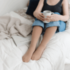 A woman wearing compression stockings sitting in bed with a mug