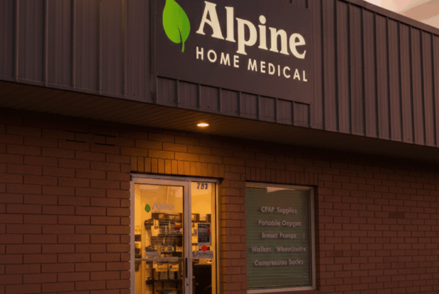 Stunning photo of the Vernal Alpine Home Medical store exterior at sunset, featuring the brightly lit green leaf logo and a beautiful, realistic sky.